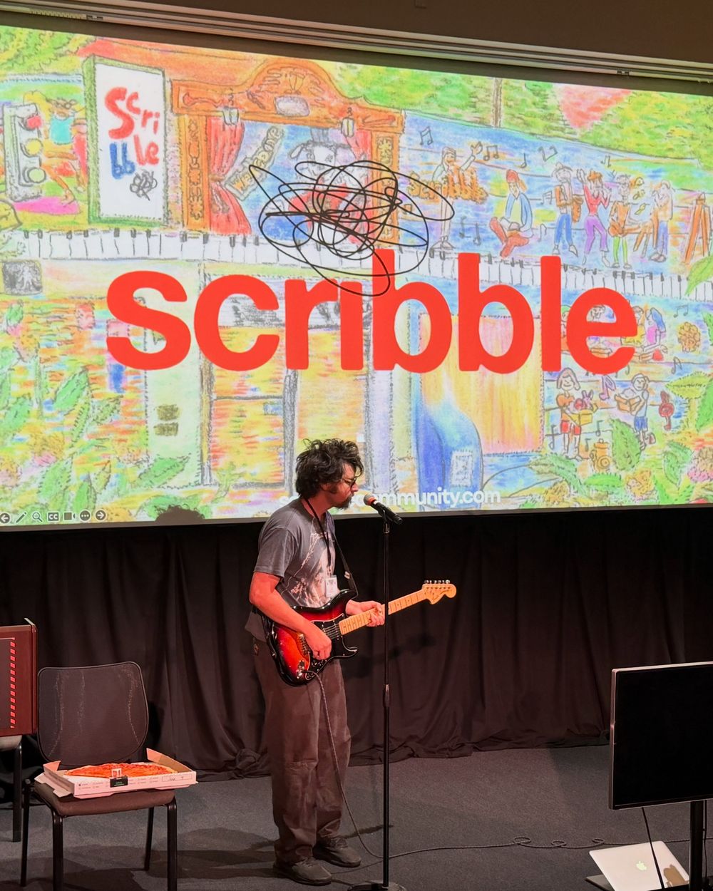 Jonny Kosmo playing electric guitar on stage in front of a colorful Scribble slide