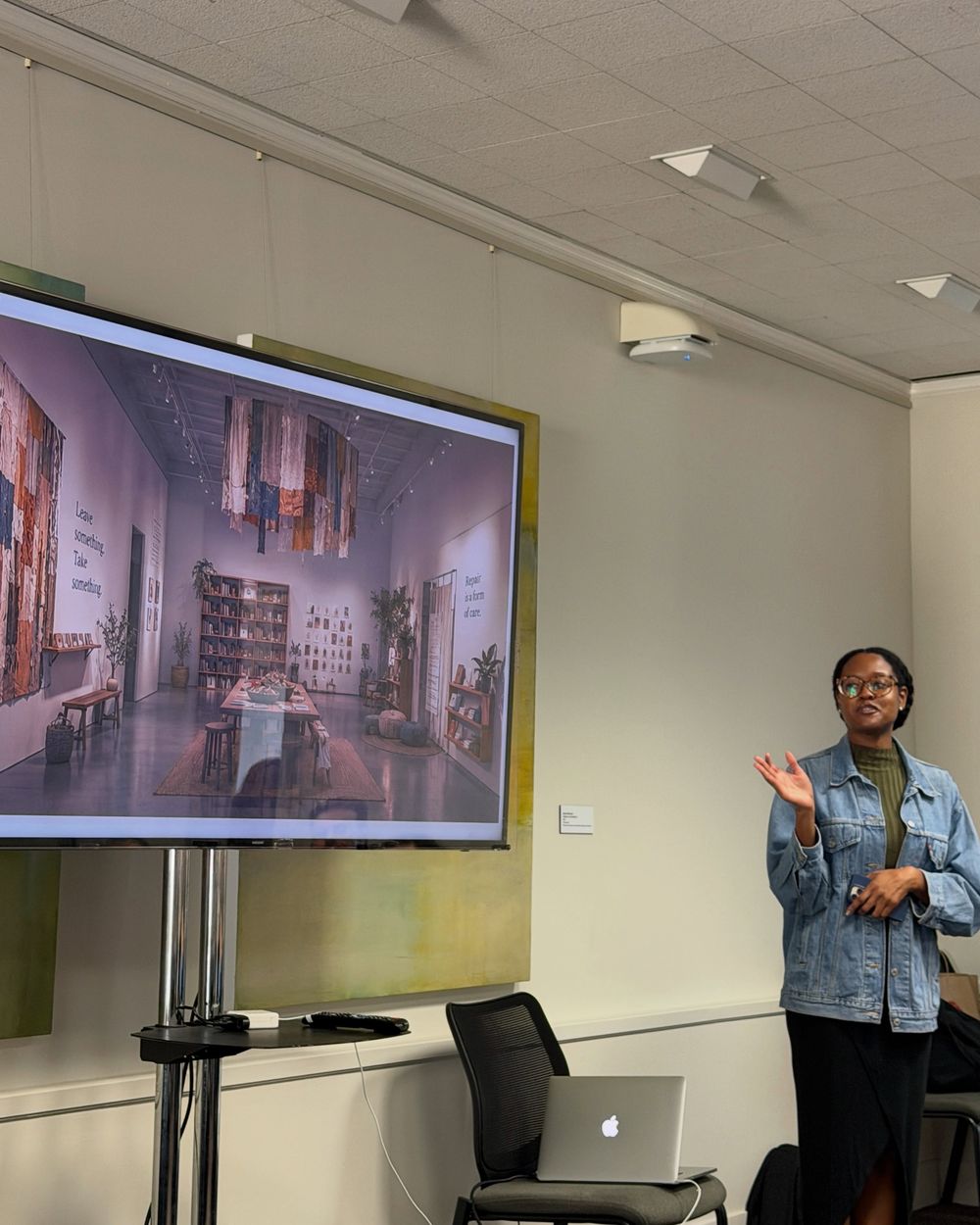 Dea Jenkins presenting beside a screen showing a textile installation